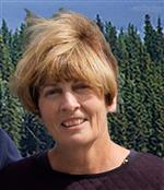 Headshot of Arlene Walker-Andrews wearing a brown shirt and standing in front of Pine trees